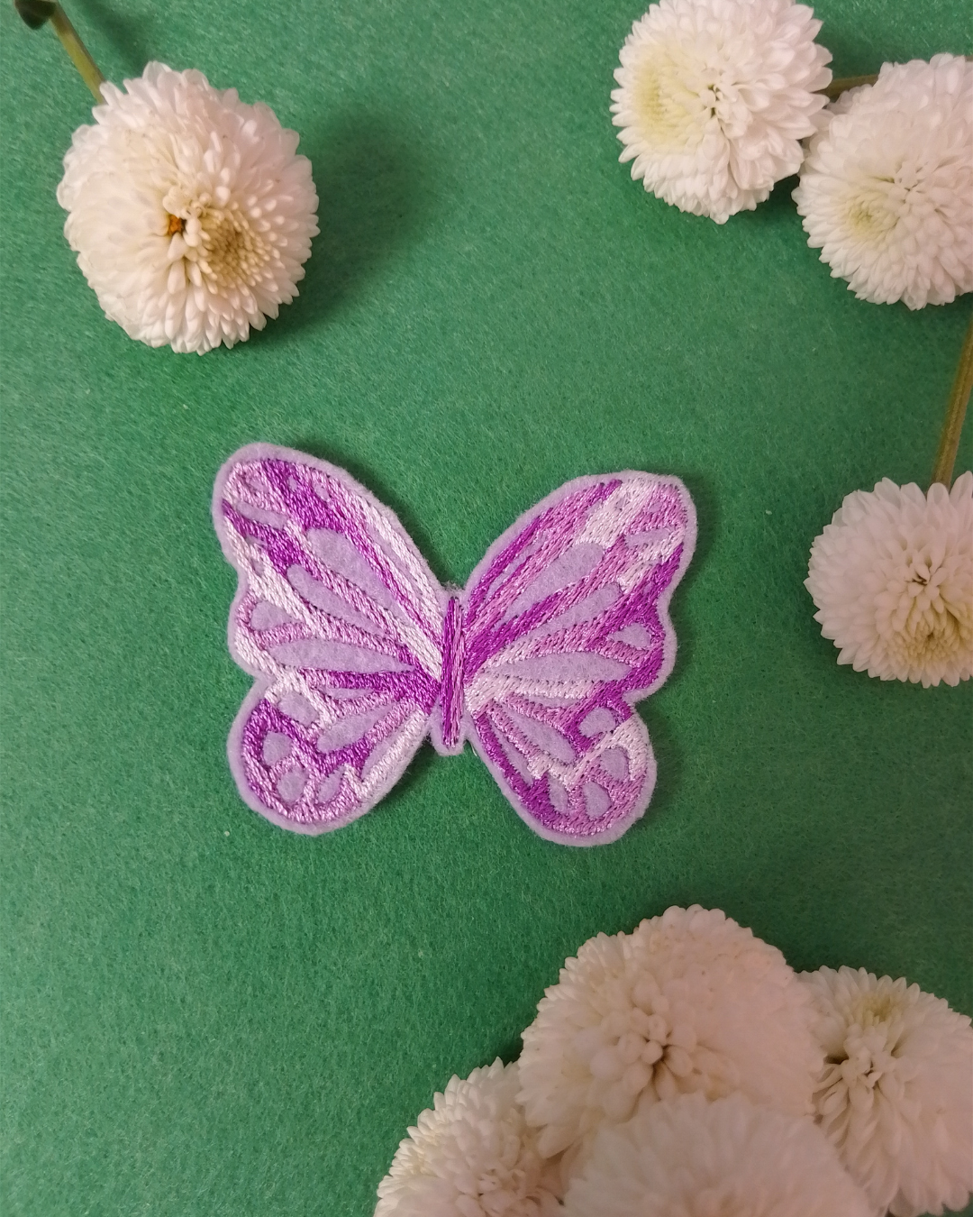 Ein Aufbügler in Form eines Schmetterlings, Stickerei in weiss und Flieder auf lila Untergrund