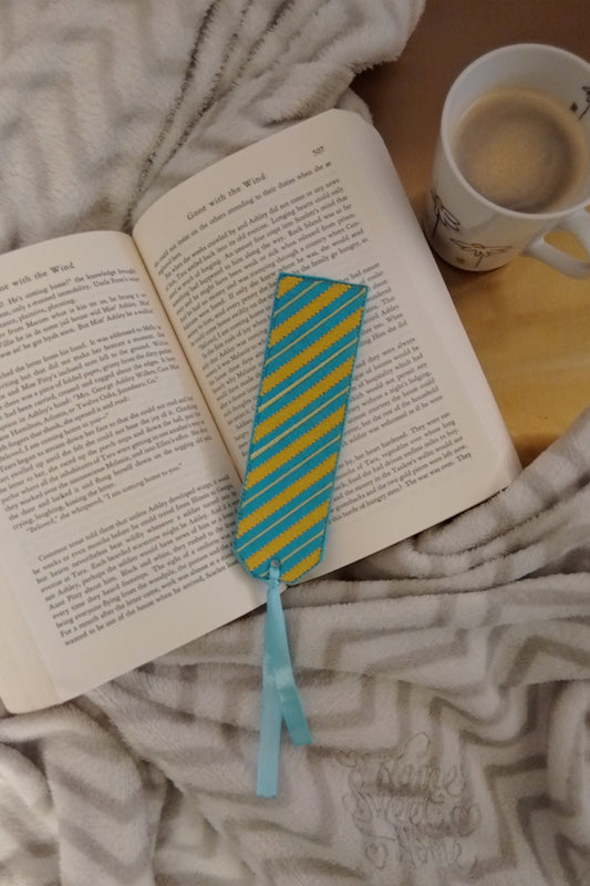 Ein türkisfarbenes Lesezeichen mit gelbe streifen in unterschiedliche Breite, präsentiert auf ein offenes Buch